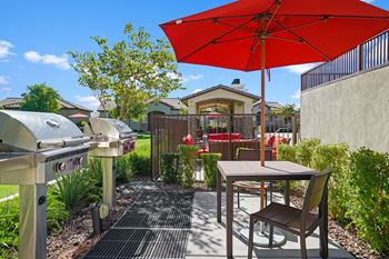 A patio with an umbrella and a table with chairs and a grill
